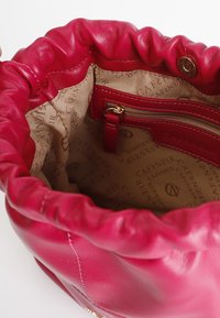 Rote Ledertasche mit gerafftem Oberteil, ausgestattet mit einem beigen Innenfutter, das mit einem Logo-Muster ausgekleidet ist, und einer Reißverschlusstasche zur Aufbewahrung.