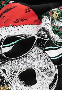 Sort stof med et grafisk design af et kranium iført solbriller, en rød julestrå hat og en grøn julekrans prydet med ornamenter.