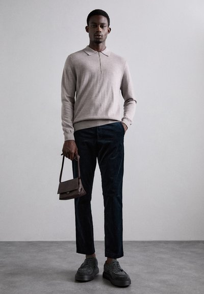 Light beige pullover with a zip collar, dark textured pants, black shoes, and a small brown handbag. Casual outfit with soft materials.