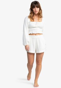 Ensemble de loungewear blanc comprenant un haut cropped avec un décolleté carré et des manches longues, associé à un short assorti. Tissu texturé, coupe décontractée.