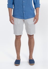 Lichtblauwe linnen shirt, witte linnen shorts en blauwe espadrilles. Opgerolde mouwen van het shirt, casual relaxte pasvorm en gestructureerde stoffen.
