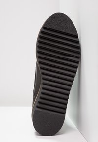 Suela de zapato negra con ranuras verticales para tracción, con una superficie texturizada y un borde redondeado. Talla 37 marcada en la suela.