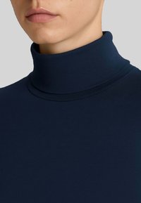 Maglione a collo alto blu navy, realizzato in un tessuto liscio e stretch con un design senza cuciture e dettagli minimalisti.