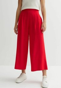 Red wide-leg trousers with a high waist and pleated front in a lightweight fabric. Paired with white sneakers on a neutral background.