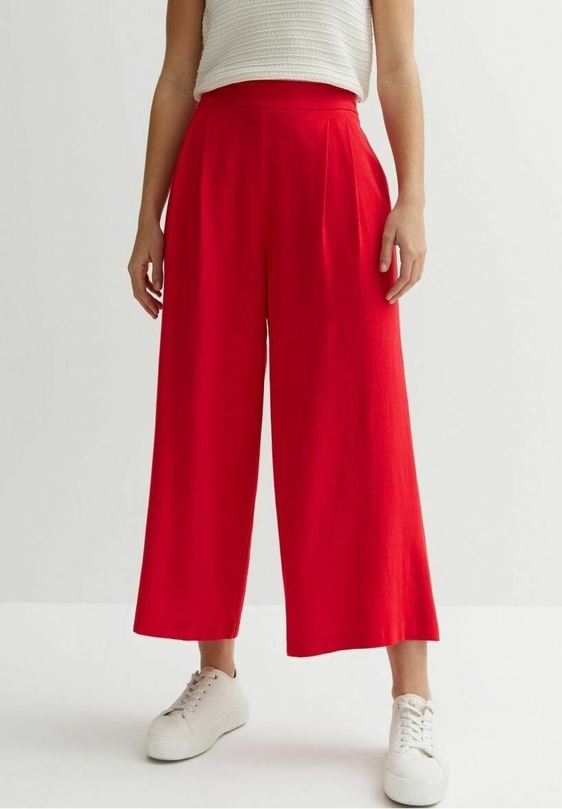 Red wide-leg trousers with a high waist and pleated front in a lightweight fabric. Paired with white sneakers on a neutral background.