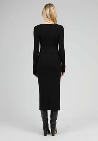 Robe noire en tricot côtelé à manches longues, ajustée et longueur cheville, associée à des bottes noires à hauteur de genoux. Texture lisse et design simple.