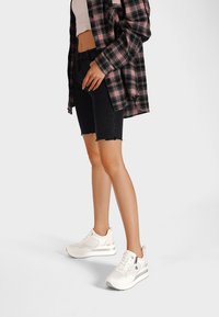 Shorts in denim nero con orlo sfrangiato, abbinati a una maglietta rosa chiaro e a una camicia a quadri nera e rosa. Sneakers bianche con accenti grigi.