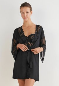 Robe in seta nera con dettagli in pizzo floreale, design a V e maniche a tre quarti. Include una cintura da annodare per una vestibilità regolabile.