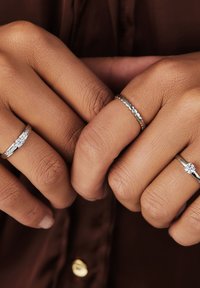 Drei silberne Ringe an Händen mit strukturierten Haut. Ein Ring hat einen zentralen Edelstein, während ein anderer ein Perlendesign aufweist.