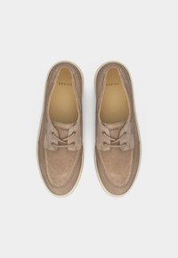 Ζευγάρι μπεζ δερμάτινα αθλητικά παπούτσια με κορδόνια και λευκές σόλες, φωτογραφημένα από πάνω σε απλό ανοιχτό φόντο.