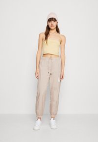Beiger, taillierter, trägerloser Oberteil, helle beigefarbene Jogginghose mit Rippbündchen und weißen Sneakern. Einfaches Design, glatte Textur und minimale Details.