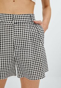 Pantalones cortos de cuadros en blanco y negro con una cintura alta, que cuentan con bolsillos laterales y un corte holgado. La tela tiene una textura suave.