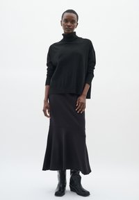 Maglione nero a collo alto abbinato a una gonna midi nera aderente. La gonna si allarga all'orlo, completata da stivali neri con tacco.