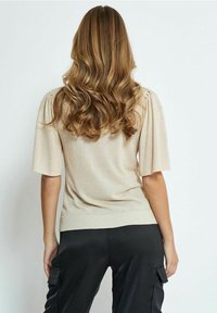 Beige top s krátkým rukávem s texturovaným povrchem a designem nabíraných ramen, doplněný o černé cargo kalhoty s bočními kapsami.