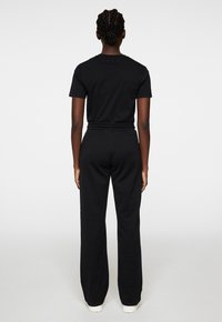 Svart bomullströja och matchande sweatpants med lös passform och elastisk midja, fotograferad bakifrån mot en enkel bakgrund.