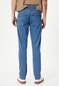 Jeans in denim azzurro chiaro con design a gamba dritta, cinque tasche e cuciture visibili. Presenta una toppa in pelle sulla vita.