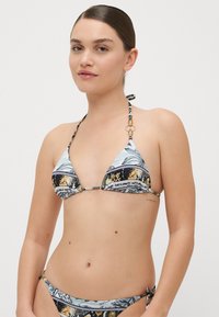 Triangelasti bikini vrh s modrim, črnim in zlatim vzorcem, ki ima halter vratne vrvice in zlate dodatke. Teksturirana tkanina z mešanimi vzorci.