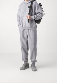 Grå hoodie och sweatpants-set, med ribbade muddar, broderad logotyp och sidosträck. Kompletterat med grå sneakers och en svart ryggsäck.