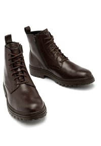 Brązowe skórzane botki za kostkę o gładkim wykończeniu, z tradycyjnymi sznurowadłami, bocznym zamkiem błyskawicznym i wytrzymałą podeszwą zapewniającą przyczepność.