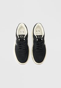 Par tenisica crne boje marke Armani Exchange s kremasto-bijelim potplatima i crnim vezicama, snimljenih iz ptičje perspektive na bijeloj pozadini.