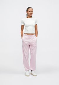 Φωτεινό πράσινο εφαρμοστό τοπ με κοντά μανίκια σε συνδυασμό με άνετο ροζ φαρδύ παντελόνι φόρμας με τσέπες και κορδόνι, ολοκληρωμένο με λευκά αθλητικά παπούτσια.