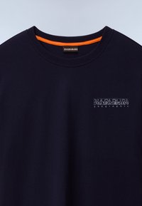 Marineblå bomuld t-shirt med rund hals, med et lille grafisk logo i lyseblå på venstre bryst og et orange detaljer indeni kraven.