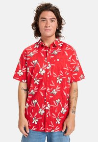 Camisa roja de manga corta con un patrón floral que presenta flores blancas y hojas verdes; diseño de botones y un bolsillo en el pecho.