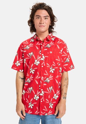 Camisa roja de manga corta con un patrón floral que presenta flores blancas y hojas verdes; diseño de botones y un bolsillo en el pecho.