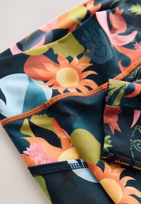 Tissu de maillot de bain avec un fond sombre présentant des motifs floraux éclatants en orange, jaune, rose et vert ; comprend des détails de couture contrastants.