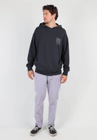 Hoodie gris foncé avec une poche avant, présentant un motif, associé à un pantalon à rayures claires et des baskets noires.