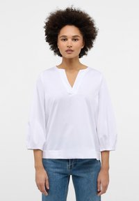 Weiße Bluse mit V-Ausschnitt, dreiviertellangen Puffärmeln und lockerer Passform. Hergestellt aus glattem Stoff, zeichnet sie sich durch minimalistische Designdetails aus.