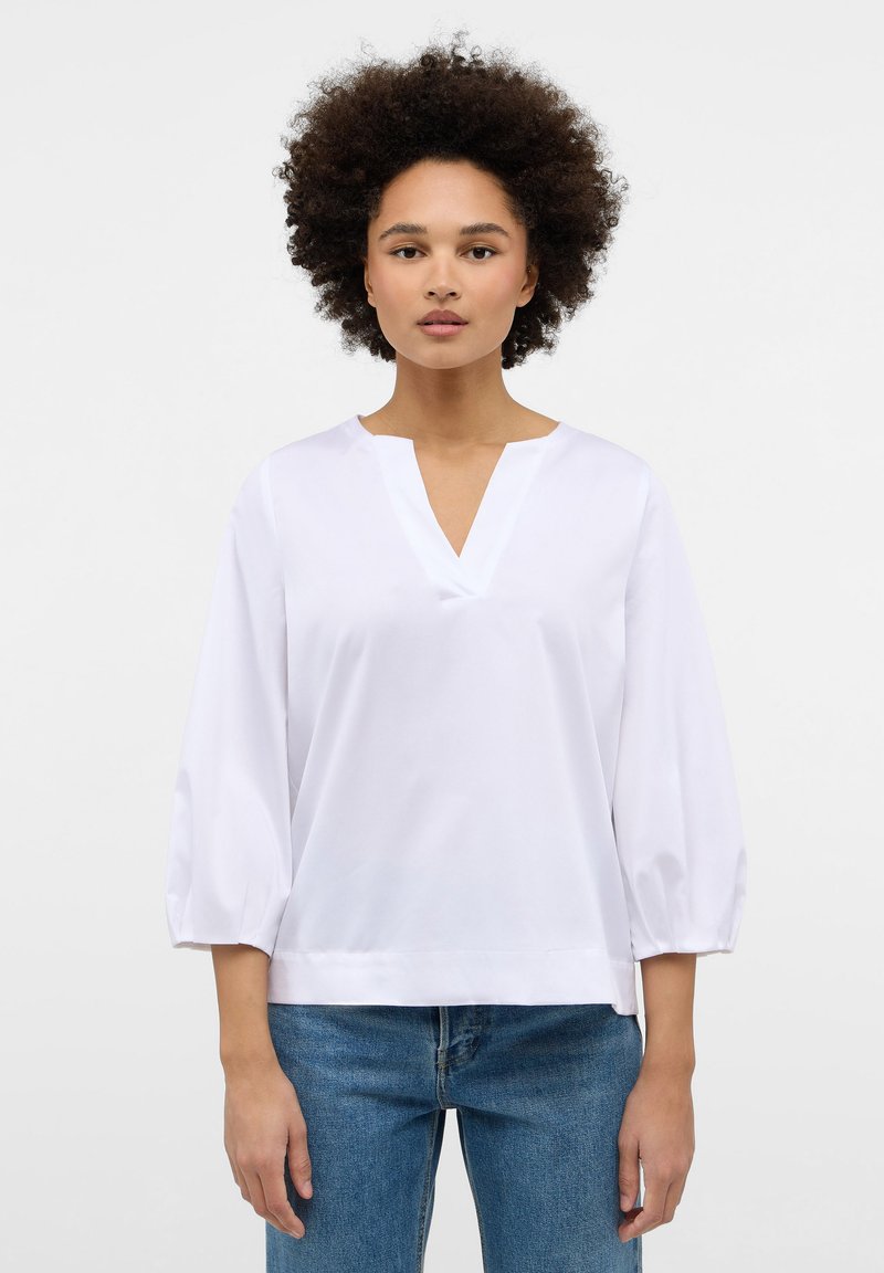 Weiße Bluse mit V-Ausschnitt, dreiviertellangen Puffärmeln und lockerer Passform. Hergestellt aus glattem Stoff, zeichnet sie sich durch minimalistische Designdetails aus.