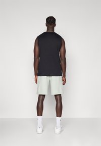 Un haut sans manches noir associé à un short vert clair, des chaussettes blanches et des baskets blanches, mettant en valeur un style décontracté et sportif.