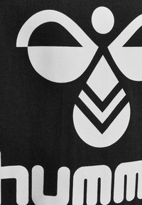 Czarny materiał z dużym białym graficznym wzorem, który przedstawia stylizowany symbol przypominający pszczołę, geometricalne kształty oraz słowo "humm" poniżej.