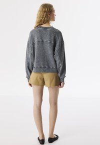 Felpa grigia oversize con una texture morbida, polsini e orlo a coste. Abbinata a pantaloni corti beige con bordi sfrangiati e scarpe nere slip-on.