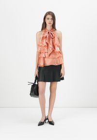 Top senza maniche in satin pesca con strati arricciati e un fiocco, abbinato a una gonna svasata in pelle nera. Accessoriato con una borsa nera.