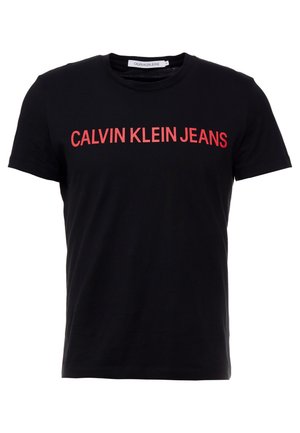 Czarna czarna koszulka z krótkim rękawem i okrągłym dekoltem z napisem „CALVIN KLEIN JEANS” w dużych czerwonych wielkich literach na wysokości klatki piersiowej.