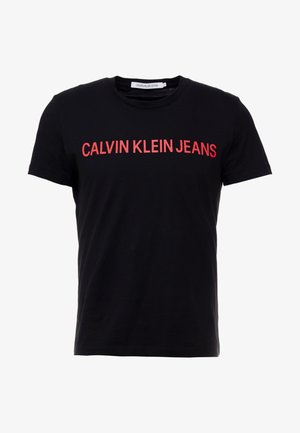 T-shirt noir à manches courtes avec col rond, arborant l'inscription "CALVIN KLEIN JEANS" en grandes lettres majuscules rouges sur la poitrine.