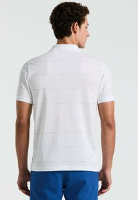 Polo blanc à manches courtes, avec de subtiles rayures horizontales multicolores. Tissu doux et lisse ; col et ourlet droit.