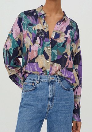 Chemise ample à boutons avec motif abstrait de visages colorés en violet, sarcelle, beige et rose, associée à un jean denim bleu taille haute.