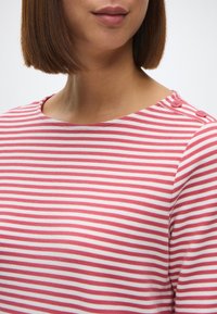 Ρ striped μπλουζάκι σε ροζ και λευκό βαμβάκι, με στρογγυλή λαιμόκοψη και κουμπιά στους ώμους. Το ύφασμα έχει μια λεία υφή με οριζόντιες ρίγες.