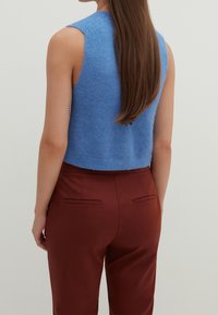 Niebieski bezrękawnik dzianinowy z okrągłym dekoltem i skróconym dołem, w połączeniu z bordowymi spodniami o dopasowanym kroju z kieszeniami bocznymi.