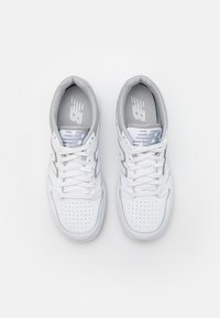 White leather sneakers with gray accents, perforated toe box, and flat white laces. Logo on the tongue and lateral side. Rounded heel design.