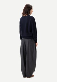 Marinblå tröja med avslappnad passform och ribbade muddar, kombinerad med löst sittande, kolgrå byxor med bakfickor och texturerat tyg.