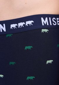 Boxer-briefs navy avec une ceinture blanche contrastante portant "MISEN". Décorés de motifs d'animaux verts et bleu clair éparpillés.