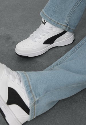 Hvit sneakers med svarte detaljer, teksturert læroverdel, rund tå, snøring og lavprofil såle. Kombinert med lyseblå jeans.