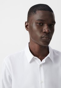 Witte button-up overhemd met een klassieke kraag, een gladde textuur en een subtiele glans, met een rechte snit en keurig afgewerkte randen.