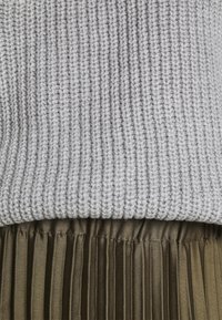 Pull en maille gris clair rentré dans une jupe plissée en satin vert olive avec une taille élastiquée.