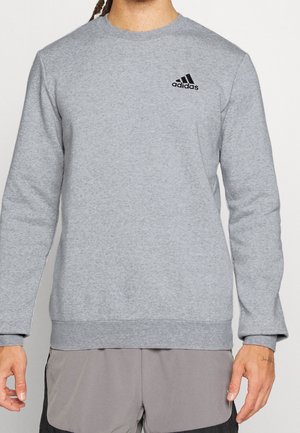 Mand iført en lysegrå Adidas-sweatshirt med sort logo på brystet og tofarvede grå shorts.