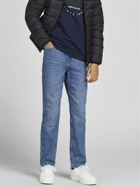 Giubbotto a vento nero, felpa blu con logo, jeans dritti blu, sneakers bianche. Texture morbide, design casual e vestibilità rilassata.